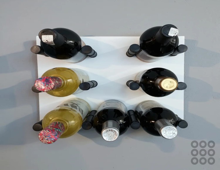 Regał wiszący na wino - system modułowy w kolorze biały mat z czarnymi szpilkami (podpórkami) na wino oraz butelkami z winem.  Widok od przodu.