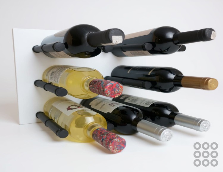 Regał wiszący na wino - system modułowy w kolorze biały mat z czarnymi szpilkami (podpórkami) na wino oraz butelkami z winem.  Widok od przodu.